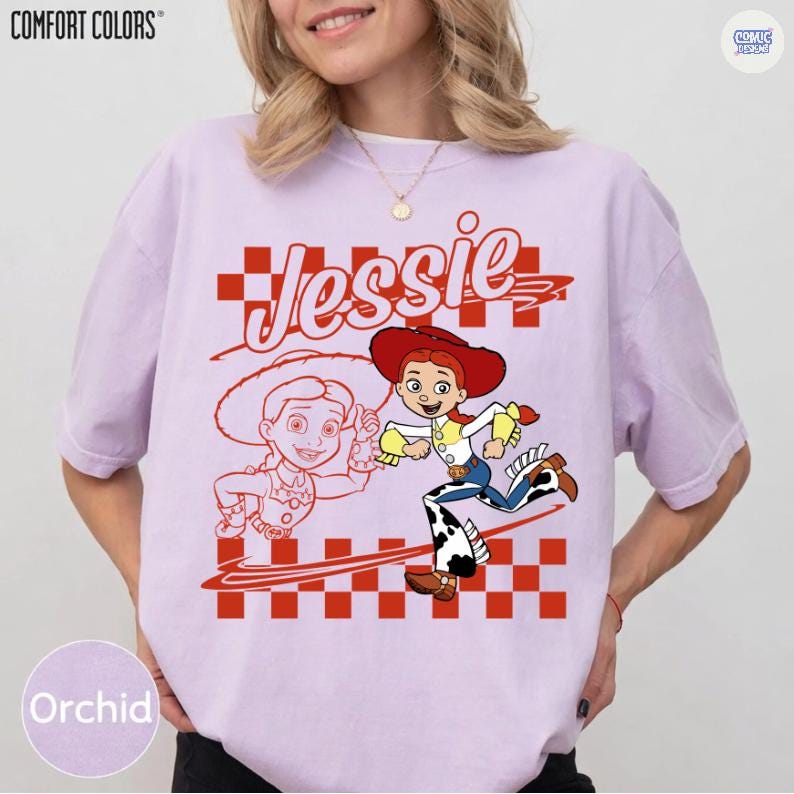 May include: A light purple short-sleeve t-shirt featuring a graphic of the character Jessie from Toy Story. The design includes the name Jessie in script, a red and white checkered pattern, and a colorful illustration of the character.