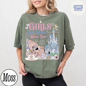 May include: Olive green t-shirt with the text "GIRLS JUST WANNA HAVE FUN" in pink and white. The graphic includes a castle, Minnie and Daisy Duck in a teacup, and other Disney-themed elements. A "Moss" logo is in the bottom left corner.