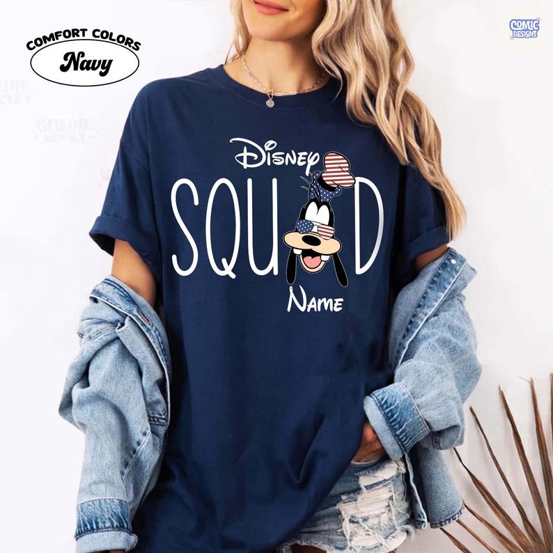 May include: Navy blue t-shirt with the words "Disney Squad" in white. The letter "D" features a cartoon character with an American flag-themed hat and sunglasses. The word "Name" is below the character. The shirt has the words "Comfort Colors" above the shirt color.