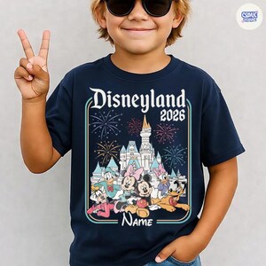 Op de afbeelding: Marineblauw T-shirt met de tekst "Disneyland 2026" en een kleurrijke afbeelding van Disney-figuren en een kasteel. Het shirt heeft een ronde hals en korte mouwen. Het woord "Name" staat onderaan de afbeelding.