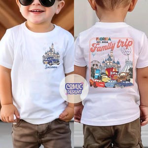 K&ouml;nnte beinhalten: Wei&szlig;es T-Shirt mit einem farbenfrohen Aufdruck eines Schlosses und eines blauen Autos, darunter der Name "Jackson". Auf der R&uuml;ckseite des Shirts befindet sich ein "Florida Family Trip"-Design mit Cartoon-Autos und einem Schloss.