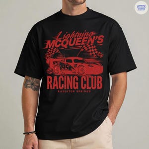 May include: Black t-shirt featuring a red graphic of Lightning McQueen's Racing Club. The design includes a race car, checkered flags, and the text "Racing Club, Radiator Springs". The shirt is a classic crew neck.