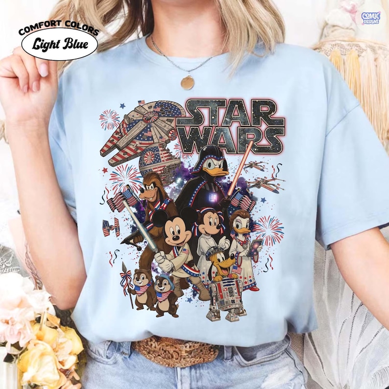 May include: Light blue Comfort Colors t-shirt featuring a Star Wars graphic with various Disney characters, fireworks, and the text "STAR WARS". The design incorporates American flag elements.