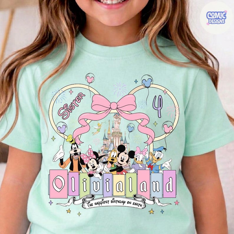 Op de afbeelding: Een lichtgroen t-shirt met een kleurrijk grafisch ontwerp. Het ontwerp bevat Disney-personages, de naam "Olivialand" en de zin "the happiest birthday on Earth". Een roze strik en het nummer "4" zijn ook inbegrepen.