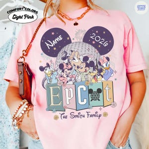 May include: Light pink Comfort Colors t-shirt featuring a Disney Epcot design. The design includes Mickey Mouse, Minnie Mouse, Donald Duck, Daisy Duck, Goofy, and Pluto. The shirt has the text "Name" and "2026" in the design, along with the text "Epcot" and "The Smith Family".