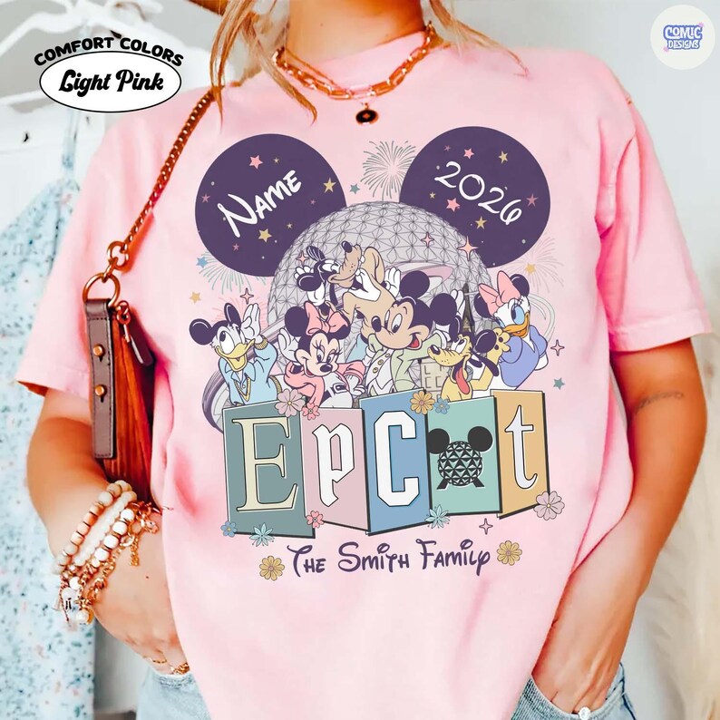 May include: Light pink Comfort Colors t-shirt featuring a Disney Epcot design. The design includes Mickey Mouse, Minnie Mouse, Donald Duck, Daisy Duck, Goofy, and Pluto. The shirt has the text "Name" and "2026" in the design, along with the text "Epcot" and "The Smith Family".