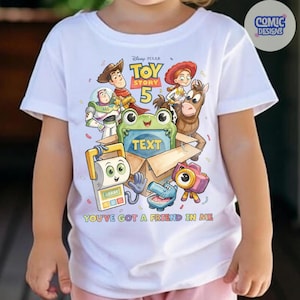 May include: A white short-sleeved t-shirt featuring a colorful Toy Story 5 graphic with characters including Woody, Buzz Lightyear, Jessie, and Bullseye. The design includes a central box with the word TEXT and the phrase YOU'VE GOT A FRIEND IN ME.