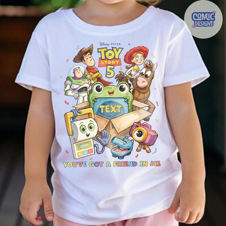 May include: A white short-sleeved t-shirt featuring a colorful Toy Story 5 graphic with characters including Woody, Buzz Lightyear, Jessie, and Bullseye. The design includes a central box with the word TEXT and the phrase YOU'VE GOT A FRIEND IN ME.