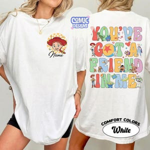 Op de afbeelding: Een wit t-shirt met een kleine afbeelding van Jessie uit Toy Story op de linkerborst met de tekst Name eronder. De achterkant toont grote kleurrijke tekst met You've Got A Friend In Me en diverse Toy Story personages.