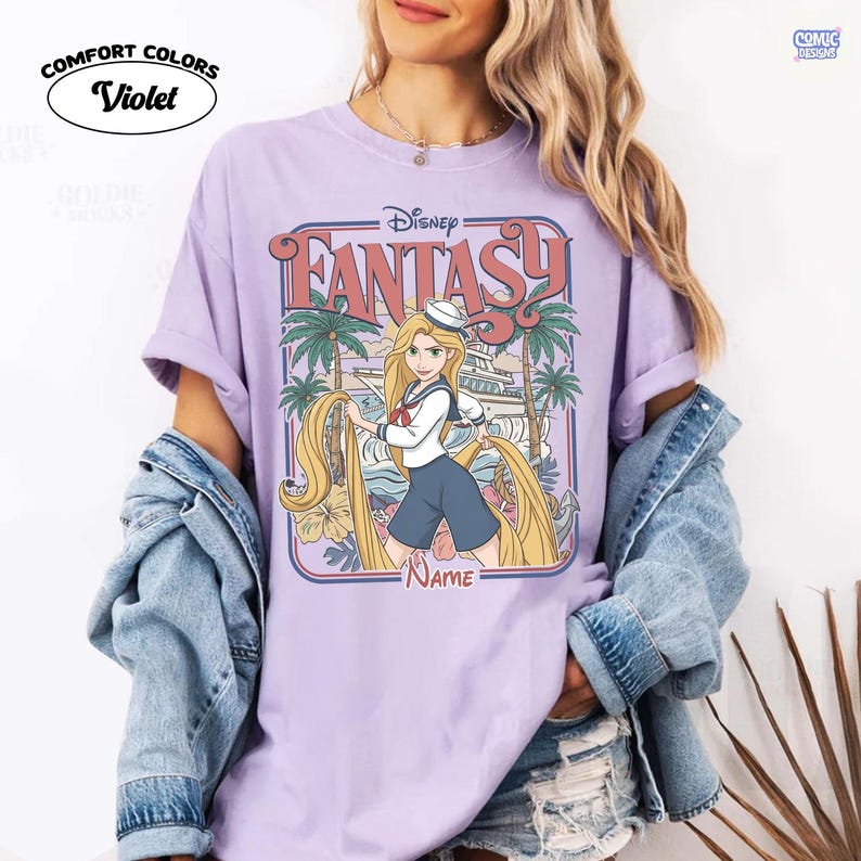 Op de afbeelding: Violet Comfort Colors T-shirt met een Disney Fantasy-ontwerp. De afbeelding toont Rapunzel met lang blond haar, palmbomen en een schip. Het shirt heeft de tekst "Disney Fantasy" en ruimte voor een naam.