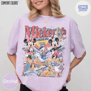 May include: Orchid-colored t-shirt with a vintage-style Mickey & Co. graphic featuring Mickey Mouse, Minnie Mouse, Donald Duck, Daisy Duck, Goofy, and Pluto. The design includes the text "Mickey & Co. Since 1928" in a retro font. The shirt has a Comfort Colors label.