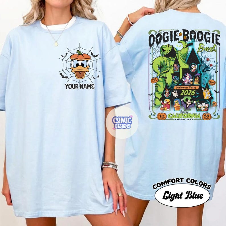 May include: Light blue t-shirts with front and back graphics. The front features Donald Duck in a pumpkin web, with the text "YOUR NAME". The back displays "OOGIE BOOGIE Bash" with Halloween characters and "2026".
