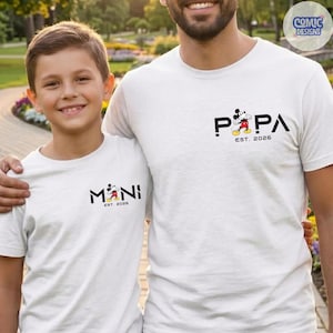May include: Two white t-shirts with matching designs. One shirt says "PAPA" with a Mickey Mouse graphic and "EST. 2026". The other shirt says "MINI" with a Mickey Mouse graphic and "EST. 2026".