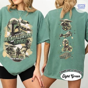 Puede incluir: Camiseta verde claro con personajes de Star Wars, The Mandalorian y Grogu. El frente presenta el casco del Mandaloriano, Grogu y texto. La parte posterior tiene gr&aacute;ficos de personajes y el texto "COMFORT COLORS Light Green."