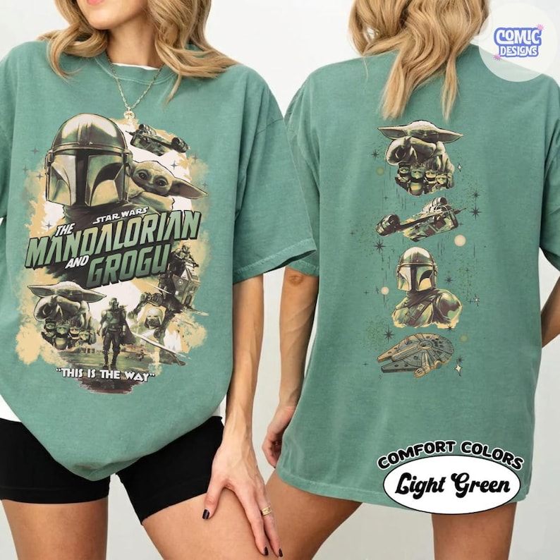 Puede incluir: Camiseta verde claro con personajes de Star Wars, The Mandalorian y Grogu. El frente presenta el casco del Mandaloriano, Grogu y texto. La parte posterior tiene gr&aacute;ficos de personajes y el texto "COMFORT COLORS Light Green."