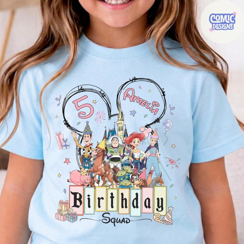 May include: Light blue t-shirt featuring a colorful graphic of Disney's Toy Story characters. The design includes the number 5, the name "Amelia", and the words "Birthday Squad". The shirt is a children's birthday theme.
