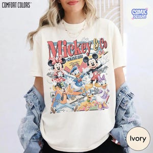 May include: Ivory-colored t-shirt featuring a vintage-style graphic of Mickey Mouse and friends. The design includes Mickey, Minnie, Donald Duck, Daisy Duck, Goofy, and Pluto, with the text "Mickey & Co. Since 1928". The shirt is a Comfort Colors brand.