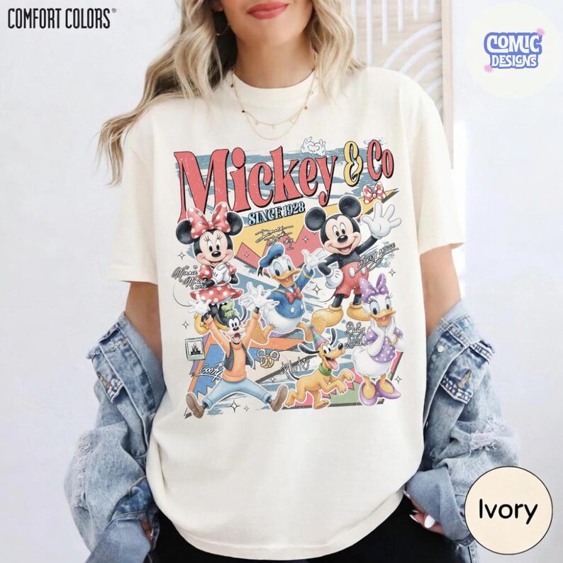 May include: Ivory-colored t-shirt featuring a vintage-style graphic of Mickey Mouse and friends. The design includes Mickey, Minnie, Donald Duck, Daisy Duck, Goofy, and Pluto, with the text "Mickey & Co. Since 1928". The shirt is a Comfort Colors brand.