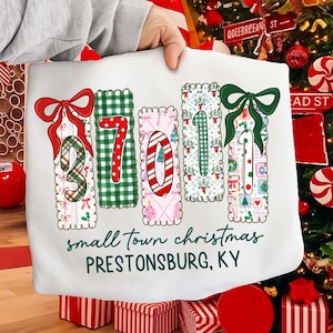 May include: White Christmas tote bag featuring the numbers "37011" in a festive design. Each number is decorated with bows, patterns, and holiday imagery. The text "small town christmas PRESTONSBURG, KY" is printed below the numbers.