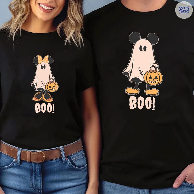 May include: Black t-shirts featuring a cartoon ghost with Mickey Mouse ears, holding a jack-o'-lantern. The ghost is wearing yellow shoes and the word "BOO!" is printed below. A matching shirt is worn by a person.