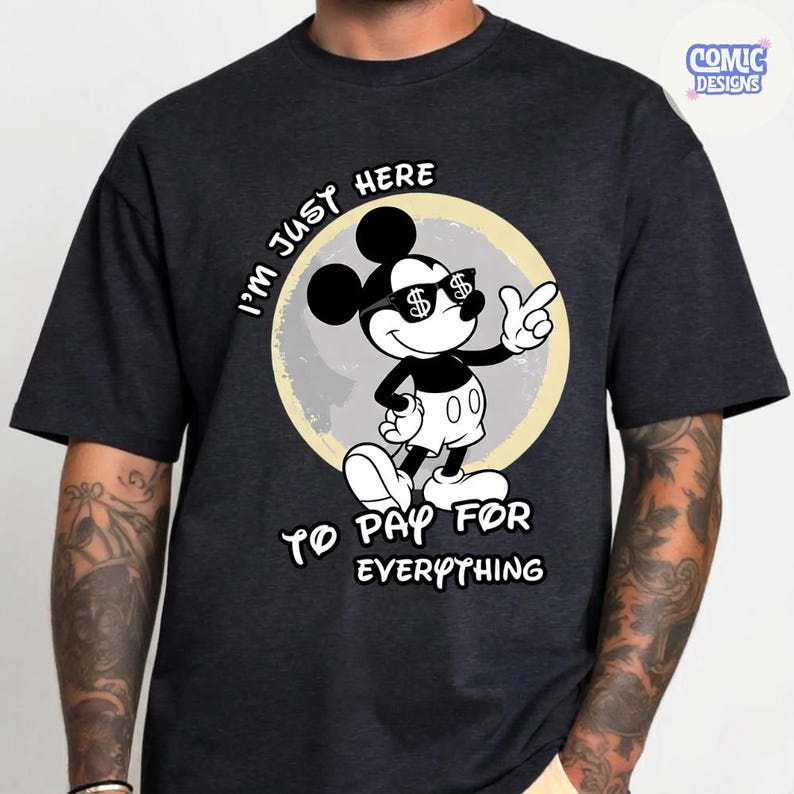 May include: Dark gray t-shirt featuring a cartoon Mickey Mouse character wearing sunglasses with dollar signs. The character is in front of a light yellow circle, with the text "I'M JUST HERE TO PAY FOR EVERYTHING".