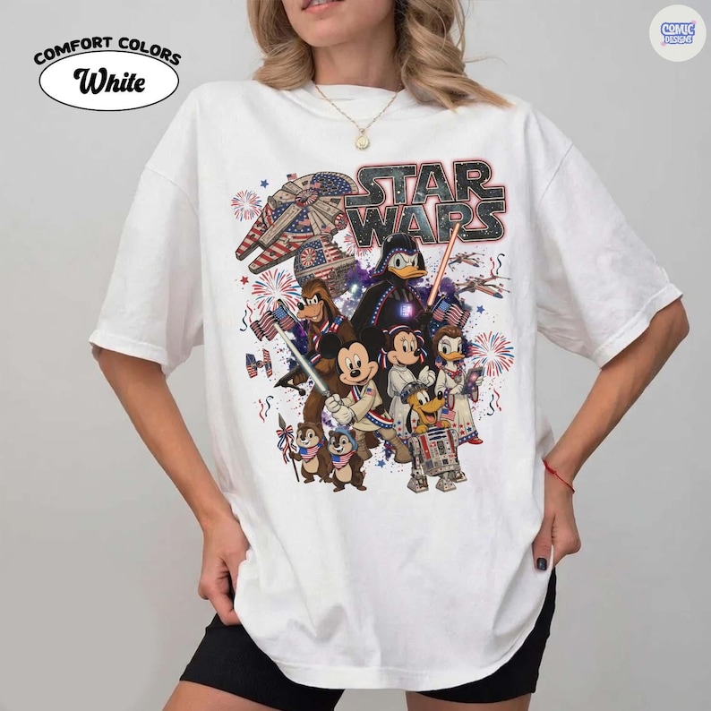 May include: White Comfort Colors t-shirt featuring a Star Wars graphic with Disney characters. The design includes Darth Vader, Mickey Mouse, Donald Duck, and others, with an American flag and fireworks theme.