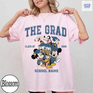 Puede incluir: Camiseta rosa claro con el texto "THE GRAD" en letras azules. La camiseta presenta un gr&aacute;fico de personajes de Disney con atuendo de graduaci&oacute;n, con el texto "CLASS OF 2026" y "SCHOOL NAME".