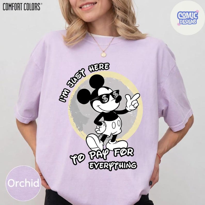 May include: Orchid-colored t-shirt with a graphic of Mickey Mouse wearing sunglasses with dollar signs. The text reads "I'M JUST HERE TO PAY FOR EVERYTHING". The shirt has the "COMFORT COLORS" and "COMIC DESIGNS" logos.
