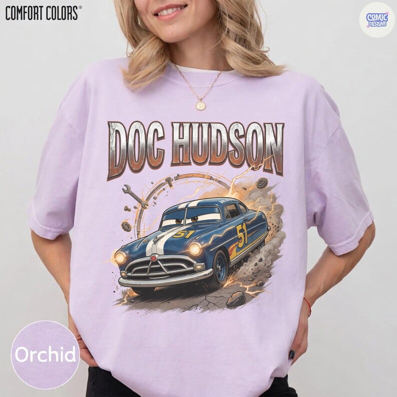 Pode incluir: Camiseta cor de orqu&iacute;dea com um gr&aacute;fico do carro de Doc Hudson do filme Carros. O design inclui o texto "DOC HUDSON" acima do carro, com o n&uacute;mero "51" do carro vis&iacute;vel. A camisa tem os logotipos "COMFORT COLORS" e "COMIC DESIGN".