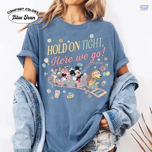 May include: Blue, Comfort Colors t-shirt with the text "HOLD ON TIGHT, Here we go!" and a cartoon roller coaster design featuring Disney characters. The shirt has rolled-up sleeves and a relaxed fit.