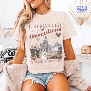 May include: Cream-colored t-shirt with the text "JUST MARRIED Disneyland" and a graphic of Mickey and Minnie Mouse in front of a castle. The shirt also features the words "Happily Ever After".
