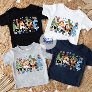 May include: Four short-sleeved t-shirts in black, white, grey, and navy blue. Each shirt features a graphic print of the word NAME with colourful cartoon characters from Toy Story integrated into the letters. A circular logo reads COMIC DESIGNS.
