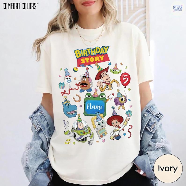 May include: An ivory t-shirt featuring a colorful graphic print with the text "BIRTHDAY STORY" and "Name" in the center. The design includes various cartoon characters wearing party hats, confetti, a red balloon with the number 5, and gifts.