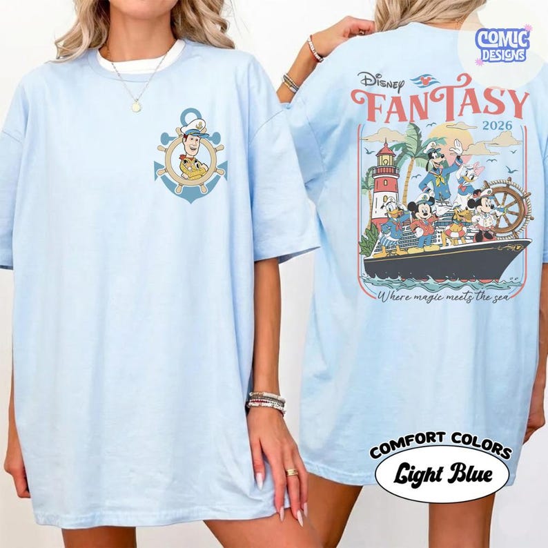 May include: Light blue t-shirt featuring a nautical-themed graphic with Woody and a ship's wheel on the front. The back of the shirt displays a Disney Fantasy cruise ship design with Mickey Mouse and friends. The text "FANTASY 2026" is also visible.