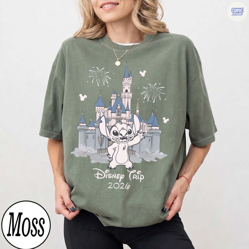 May include: Olive green t-shirt featuring a graphic of Stitch in front of a castle with fireworks and the text "Disney Trip 2026". The shirt has a crew neck and short sleeves. The brand logo "Moss" is in a circle at the bottom.