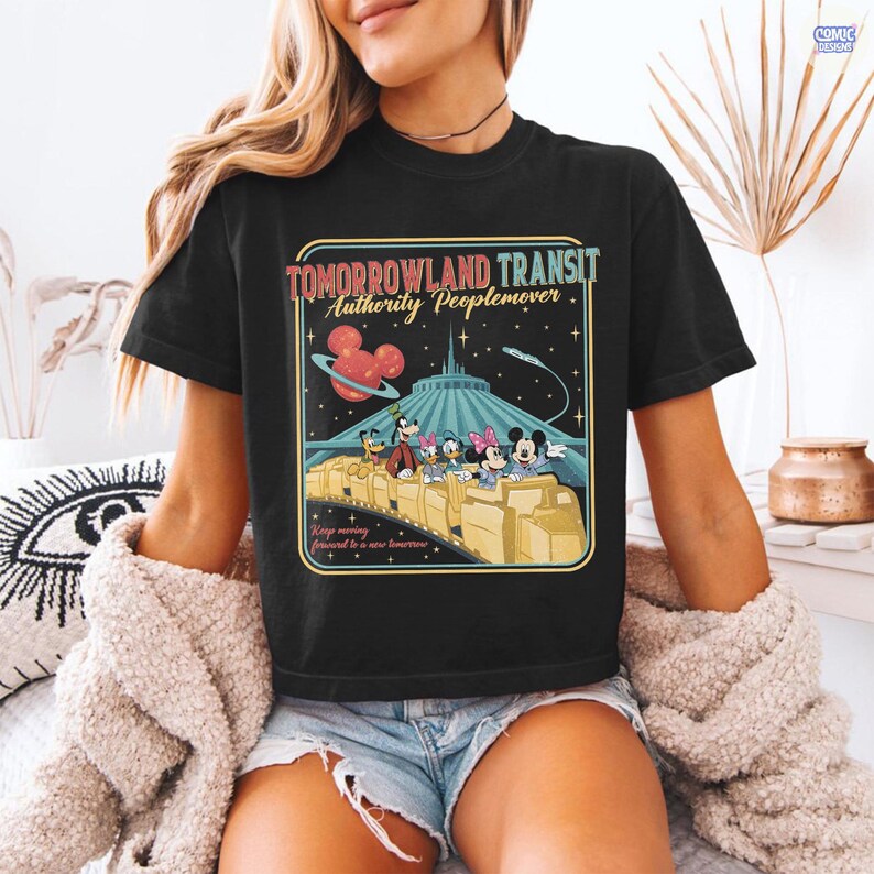 Puede incluir: Camiseta negra con un dise&ntilde;o gr&aacute;fico de estilo retro de la atracci&oacute;n Tomorrowland Transit Authority Peoplemover, con Mickey Mouse y sus amigos. El dise&ntilde;o incluye el texto "Tomorrowland Transit Authority Peoplemover" y "Keep moving forward to a new tomorrow."