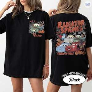 May include: A black t-shirt featuring a front graphic of a green tow truck with spiderwebs and pumpkins, and a back graphic with the text Radiator Springs and Trunk or Treat, displaying multiple cartoon cars in Halloween costumes and pumpkins.