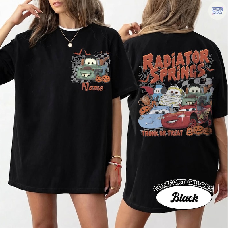 May include: A black t-shirt featuring a front graphic of a green tow truck with spiderwebs and pumpkins, and a back graphic with the text Radiator Springs and Trunk or Treat, displaying multiple cartoon cars in Halloween costumes and pumpkins.