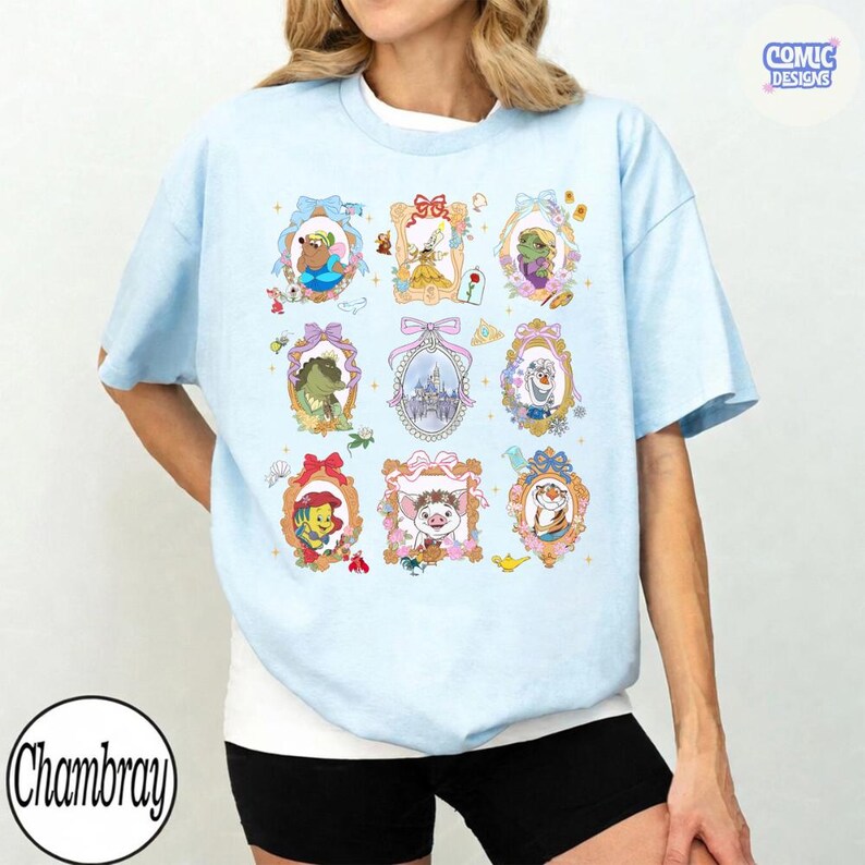 Puede incluir: Camiseta azul claro con retratos enmarcados de personajes de dibujos animados. La camiseta tiene cuello redondo y mangas cortas. El texto "Comic Designs" est&aacute; en la esquina superior derecha y "Chambray" en la esquina inferior izquierda.