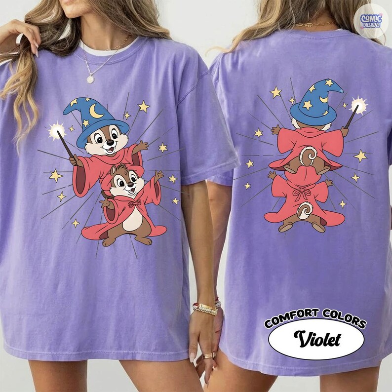 Puede incluir: Una camiseta lila Comfort Colors con un dibujo animado de dos ardillas listadas vestidas de magos, con sombreros azules y t&uacute;nicas rojas. La parte trasera de la camiseta muestra el mismo dise&ntilde;o. El texto "COMFORT COLORS Violet" est&aacute; impreso en la parte inferior.