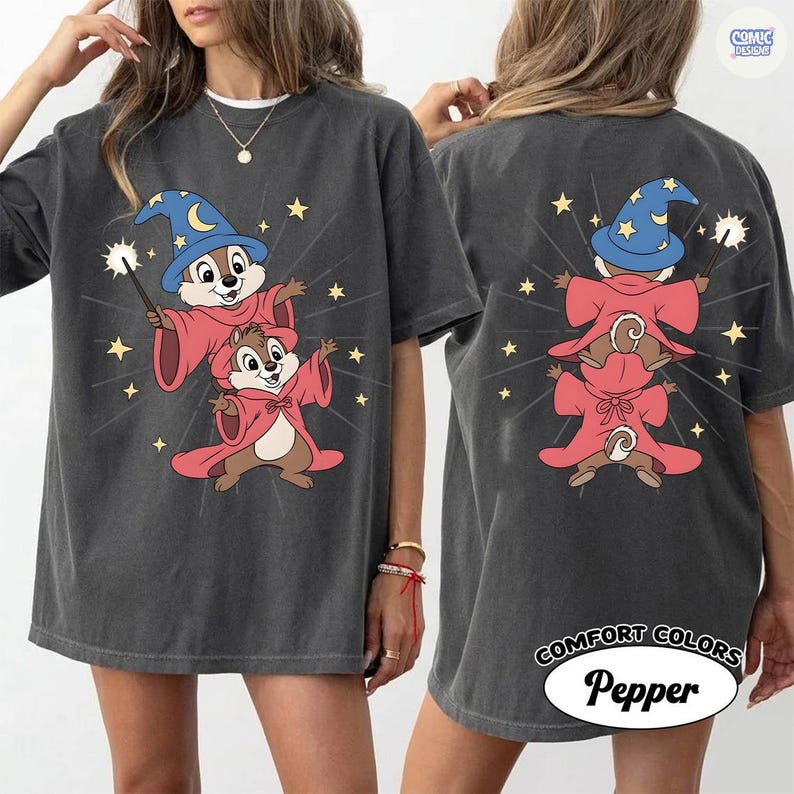 Puede incluir: Camiseta gris oscuro con una ilustraci&oacute;n de dibujos animados de dos ardillas listadas vestidas de magos, una con un sombrero azul y una varita. El dise&ntilde;o incluye estrellas y est&aacute; impreso en la parte delantera y trasera. La camiseta est&aacute; etiquetada como "Comfort Colors Pepper".