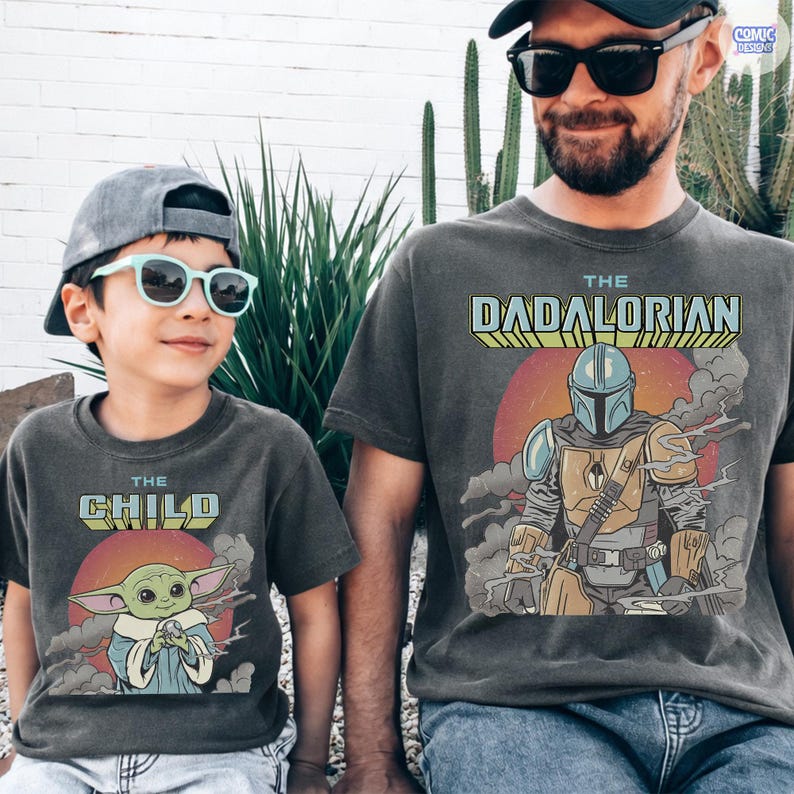 Puede incluir: Dos camisetas grises carb&oacute;n a juego. Una dice "The Child" con un gr&aacute;fico de Grogu, la otra dice "The Dadalorian" con un gr&aacute;fico mandaloriano. Ambas camisetas tienen un aspecto vintage y desgastado y las llevan un ni&ntilde;o y un adulto.