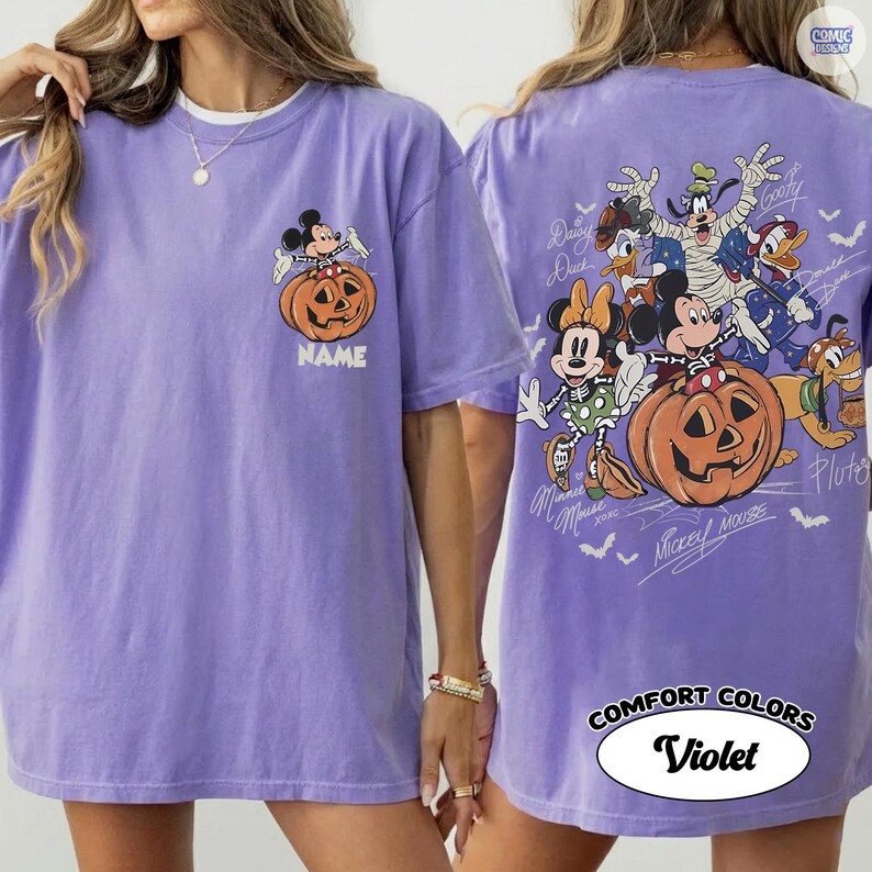May include: A violet t-shirt featuring a small graphic on the front left chest of Mickey Mouse sitting on a pumpkin with the text NAME. The back displays a large graphic of various cartoon characters in costumes with pumpkins and bats.