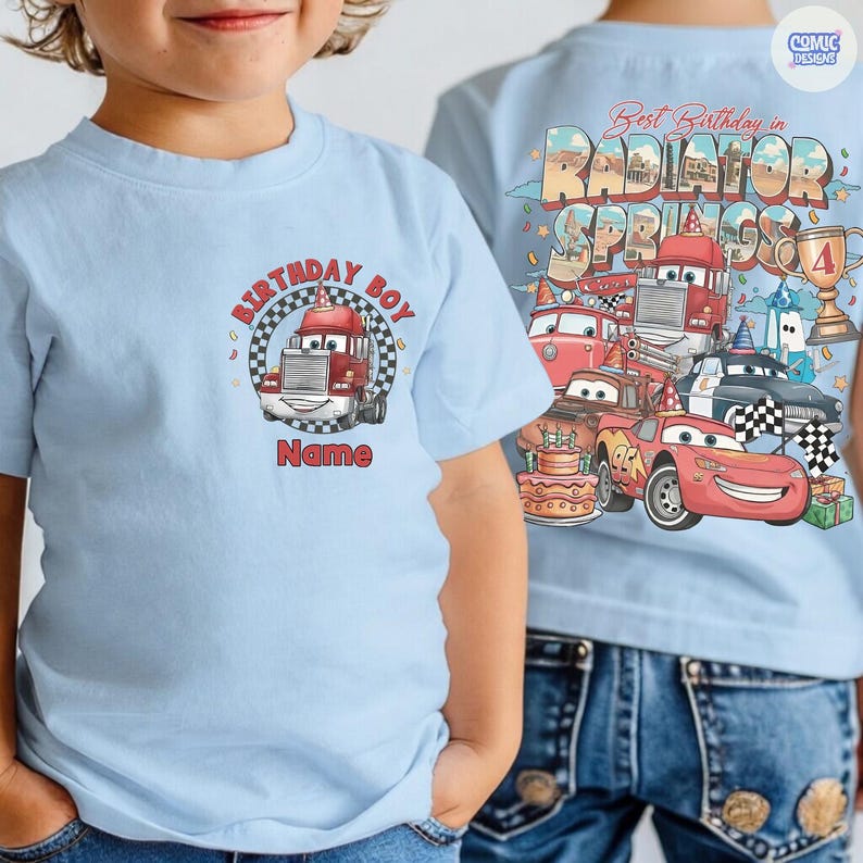 May include: Light blue t-shirt featuring a cartoon truck with the text "Birthday Boy" and "Name" on the front. The back of the shirt displays a colorful graphic with the text "Best Birthday in Radiator Springs" and various cartoon cars.