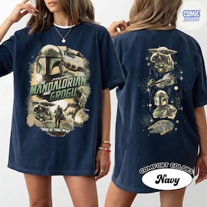 Puede incluir: Camiseta azul marino con gr&aacute;ficos de The Mandalorian y Grogu. La parte delantera muestra el casco del Mandaloriano y Grogu, con el texto "The Mandalorian and Grogu" y "This is the Way". La parte trasera muestra ilustraciones de personajes y naves.