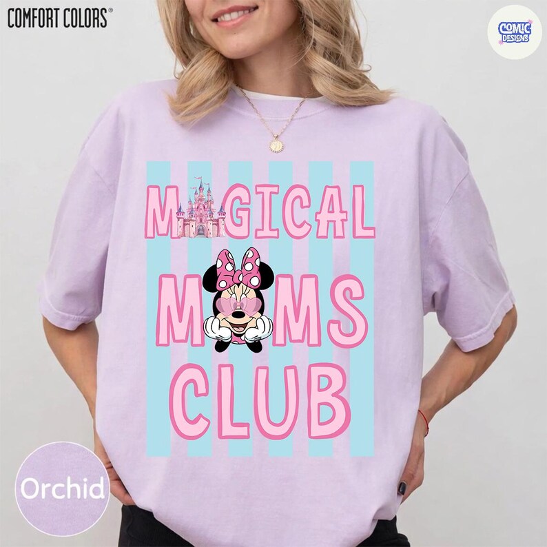 K&ouml;nnte beinhalten: Orchideenfarbenes T-Shirt mit den Worten "MAGICAL MOMS CLUB" in Pink, mit einer Minnie Mouse Grafik. Das Design beinhaltet ein Schloss und blaue vertikale Streifen. Das Shirt ist von Comfort Colors.