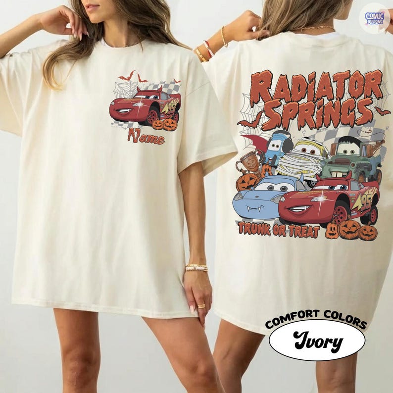 May include: An ivory t-shirt featuring a red race car with devil horns and pumpkins on the chest. The back displays multiple cartoon cars in Halloween costumes, spider webs, and the text Radiator Springs Trunk or Treat in orange font.