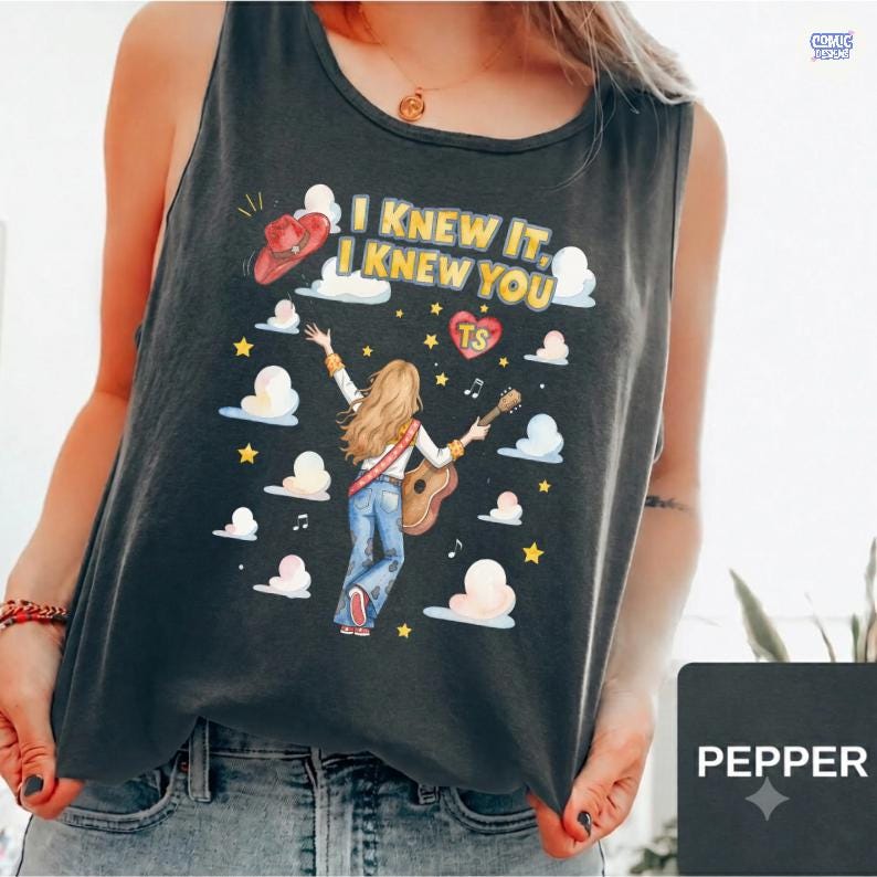 May include: A charcoal gray sleeveless tank top featuring a graphic illustration of a person with long hair playing an acoustic guitar. The design includes clouds, yellow stars, a red cowboy hat, and the text I KNEW IT, I KNEW YOU with a heart.