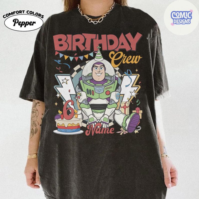 May include: Black Comfort Colors t-shirt featuring a colorful graphic of Buzz Lightyear from Toy Story. The design includes the text "BIRTHDAY Crew" and "6" on a cake, with space for a name. The shirt has a vintage look.