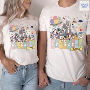 May include: White t-shirts with a colorful graphic featuring Disney characters, a castle, balloons, and the text "PreK Grad." One shirt says "Mommy" and the other says "Daddy."